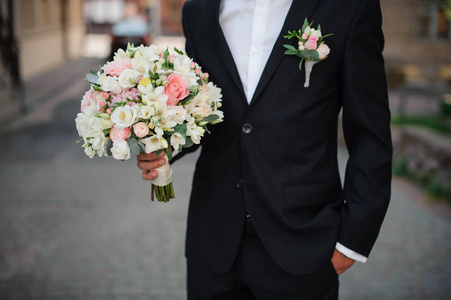 穿着黑色西装的新郎捧着一束温柔的婚礼花束