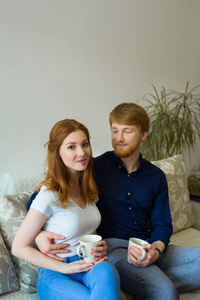 一对漂亮的年轻夫妇，一对红头发的男人和女孩坐在沙发上喝茶
