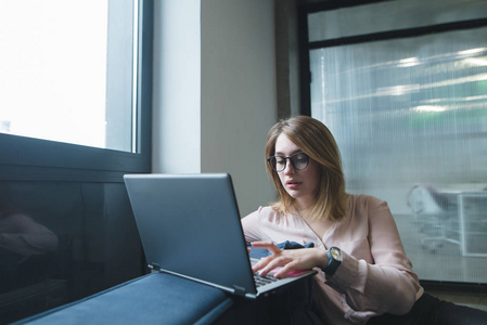 一个漂亮的年轻女人在办公室的沙发上使用笔记本电脑。自由职业者在 coworking 工作