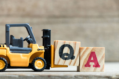 玩具黄色叉车举行字母块 Q 完成字 Qa 质量保证简称或常见问题 在木头背景