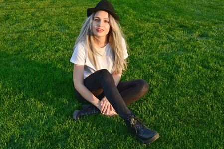 穿着黑帽子坐在绿草地上，满脸笑容的时髦迷人的年轻女子