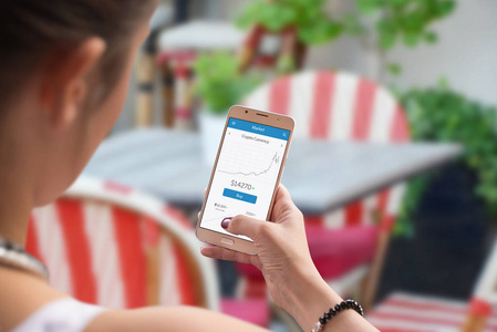 新的虚拟货币统计在手机屏幕上的女性手。 背景的咖啡店或餐馆。
