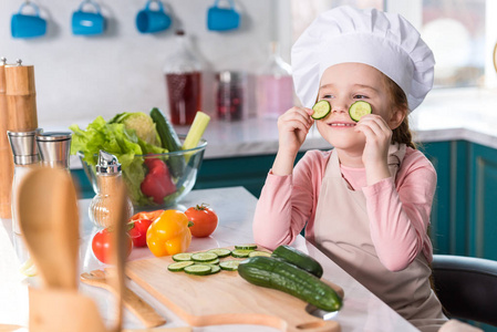 厨师帽和围裙的孩子在厨房做饭时拿着黄瓜片