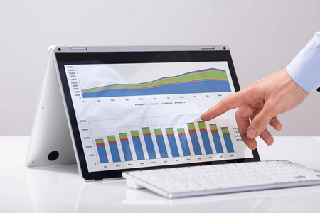 s Hand Pointing On The Chart Over Hybrid Laptop Screen With Keyb