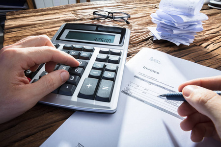 s Hand Calculating Invoice With Calculator On Wooden Desk