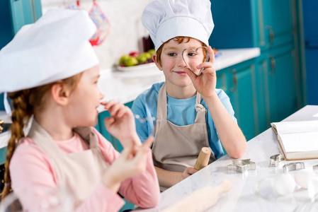 可爱的孩子们戴着厨师帽和围裙，在厨房一起做饭时互相微笑