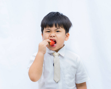 肖像可爱的亚洲男孩吃红草莓白色 backgroun