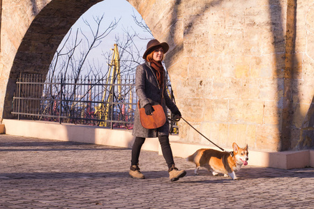 戴帽子的年轻女子和可爱的科吉狗在公园散步，阳光明媚的秋日