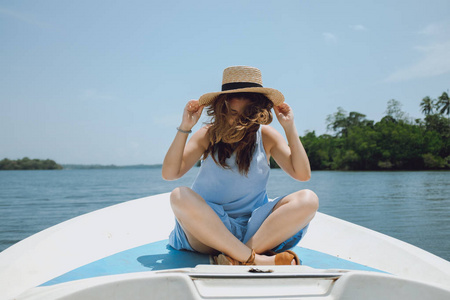 年轻的女人坐在船的前面, 用她的手握住帽子