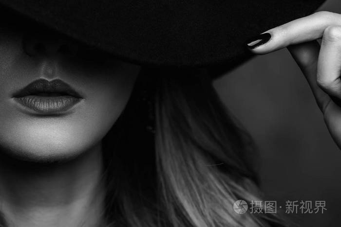 美丽的年轻神秘的金发女孩在黑色的帽子和黑色夹克灰色背景.