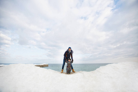 妇女在海雪海滩背景与小逗人喜爱孩子男孩在工作服用玩具汽车, 铁锹。妈妈, 孩子们在冬天的时候很开心。家庭假日, 5月15日, 爱