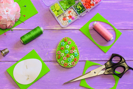 明亮的复活节彩蛋装饰与塑料花和珠子。 毡蛋工艺品剪刀线纸模板顶针上的紫色木制背景。 孩子们的缝纫项目。 手工缝纫项目。 初学者的
