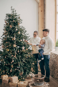 一对年轻夫妇和一个小男孩站在圣诞树旁的画像