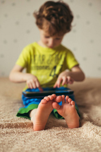 孩子们坐在床上看卡通片。有选择地关注脚部。穿着绿色 t恤和蓝色裤子的可爱男孩。垂直照片