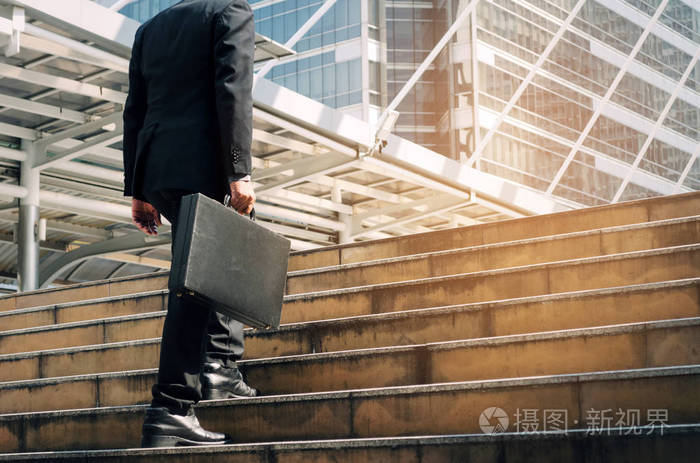 年轻英俊的商人拿着公文包,走上楼梯,早上上班时间在