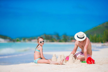 在热带白色海滩的家庭制作沙子城堡。在热带海滩上玩沙子的父亲和女孩