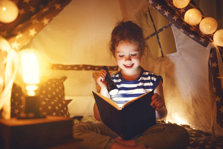 愉快的孩子女孩笑和读书书在黑暗在帐篷在 ho