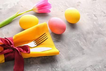 装饰精美的餐具和彩绘鸡蛋，用于灰色背景的复活节餐桌