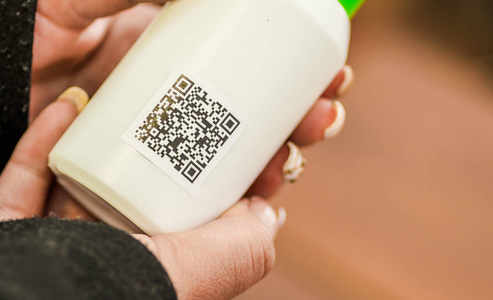 在一个模糊的背景下, 用 Qr 码信息在一个空塑料瓶上显示一个女人的手