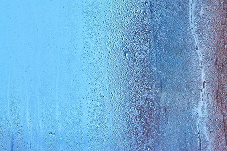 天然水滴背景。 窗玻璃具有冷凝高湿度大液滴流下来的冷色调。 收集和向下流动