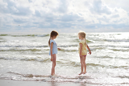 两个小妹妹在温暖和阳光明媚的夏日在沙滩上玩得很开心。 孩子们在海边玩。 儿童暑期活动。
