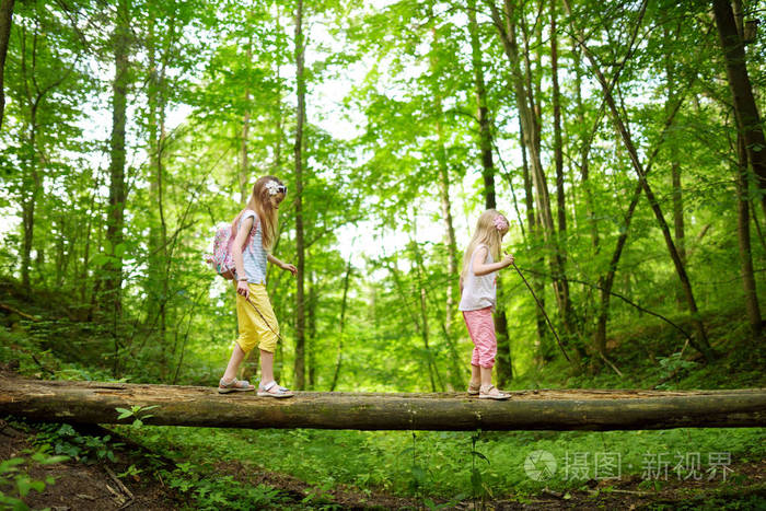 两个可爱的小妹妹在美丽的夏日森林徒步旅行中玩得很开心.