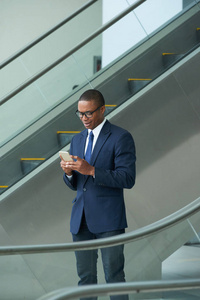 非裔美国商人站在自动扶梯上，读着他的智能手机留言