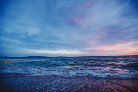 海滩上的粉红色日落。黄昏时分有波浪的海滩