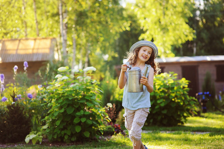 在阳光明媚的夏日花园里，戴着园丁帽的快乐有趣的小女孩在玩水缸