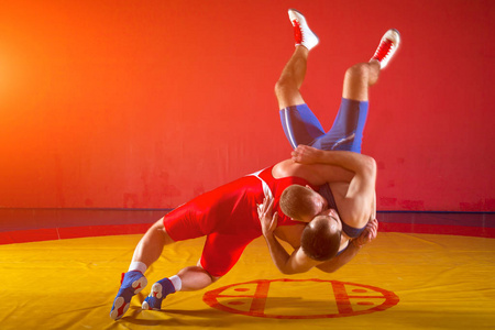 两位身穿红蓝制服的罗马摔跤手在体育馆的黄色摔跤地毯上摔跤
