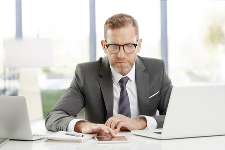 中年金融顾问商人在办公室坐在办公桌前工作,在制作数字平板电脑.照片