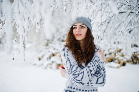 可爱的卷发女孩在雪地森林公园的毛衣和帽子