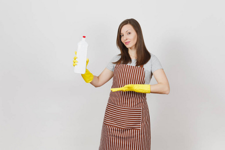 年轻的主妇穿着黄色的手套, 条纹的围裙被隔离在白色的背景上。妇女手持和指着手在瓶子上清洗和清洁的液体。复制广告空间
