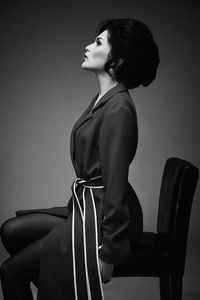 黑白照片，华丽的年轻女子，穿着时尚的外套，坐在椅子上，在工作室的背景下。