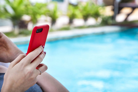在游泳池附近的休息室里坐着一个女孩，带着现代移动电话