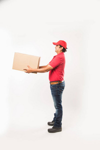 送货概念肖像快乐印度或送货员穿红色或绿色制服步行或跳跃，检查或呈现纸板箱与复制空间。