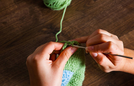 女人的手在木制背景上用钩针编织照片