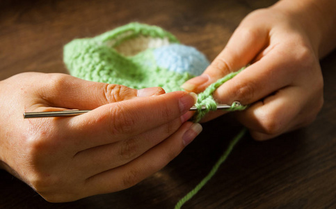 女人的手在木制背景上用钩针编织照片