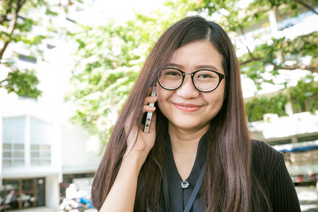 年轻的商界亚裔女性在绿色公园使用手机，传播概念