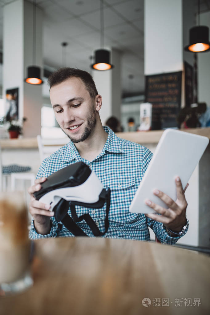 年轻的帅哥坐在网吧里用虚拟现实耳机或眼镜