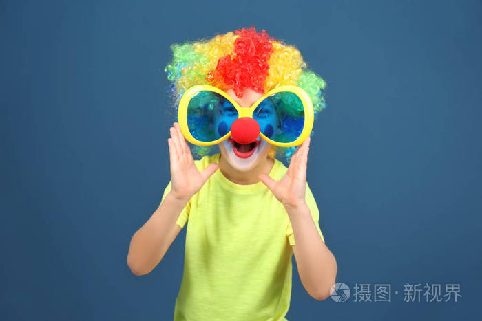 可爱的小男孩与小丑化妆在大眼镜的颜色背景.愚人节庆典