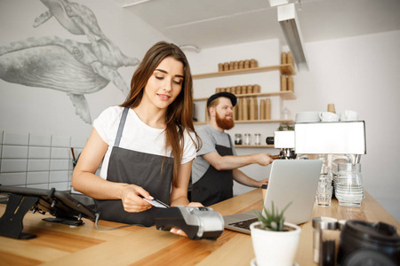 咖啡商业理念美丽的女咖啡师为客户提供信用卡服务, 并在现代咖啡馆的酒吧柜台工作时微笑。