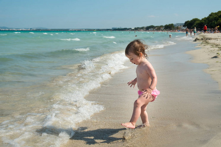 可爱的小女孩在粉红色的 swimsuite 漫步在海滩上