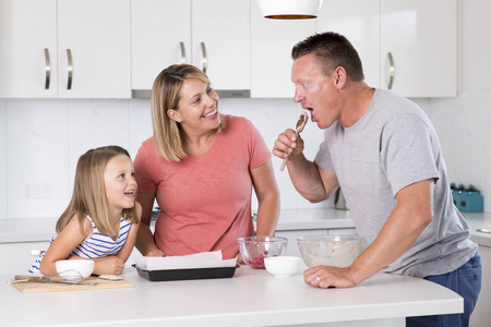年轻幸福夫妇一起烘烤与年轻漂亮的女儿在家厨房玩奶油在家庭生活的乐趣
