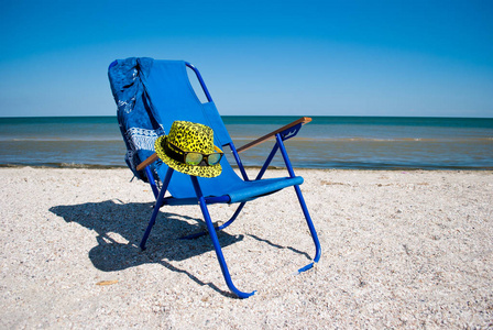 蓝色的沙滩椅和带太阳镜的时尚黄帽子在蔚蓝的大海蓝天白云美丽的风景暑假沙滩周末休息海岸