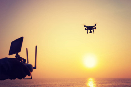 手持遥控器的女性剪影一架在日出海面上拍照的飞行无人机照片