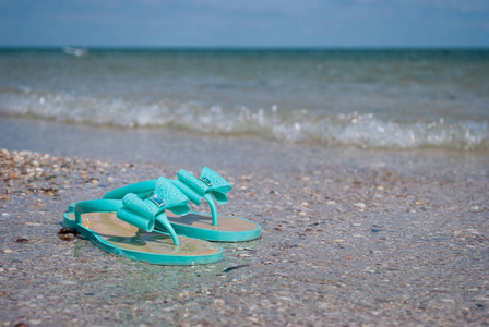 绿色海波薄荷橡胶球鞋带蝴蝶结和莱茵石沙滩拖鞋在蔚蓝的海面上，清澈的海水，贝壳，沙滩，蓝天，海浪，大风，暑假周末