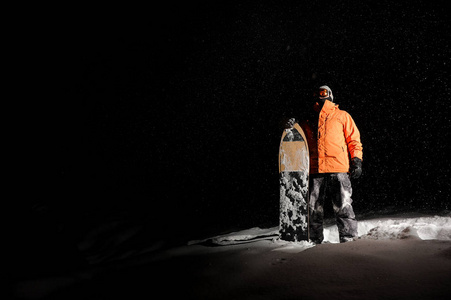 男性滑雪板在橙色运动服站立与板在雪在晚上