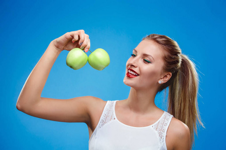 美丽的年轻健身女人幸福的微笑保持绿色苹果。健康的生活方式孤立在蓝色背景的照片