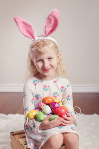 可爱的高加索儿童女孩穿着复活节兔子耳朵坐在室内工作室的木箱上。 节日彩蛋庆祝基督教传统节日
